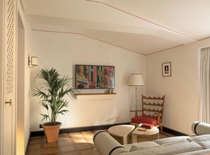 Et hotelværelse med seng, stol, bord, en potteplante, et billede og en lampe.