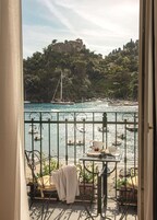 Un balcone con vista su una cittadina costiera, che include un castello su una collina e barche sull'acqua.