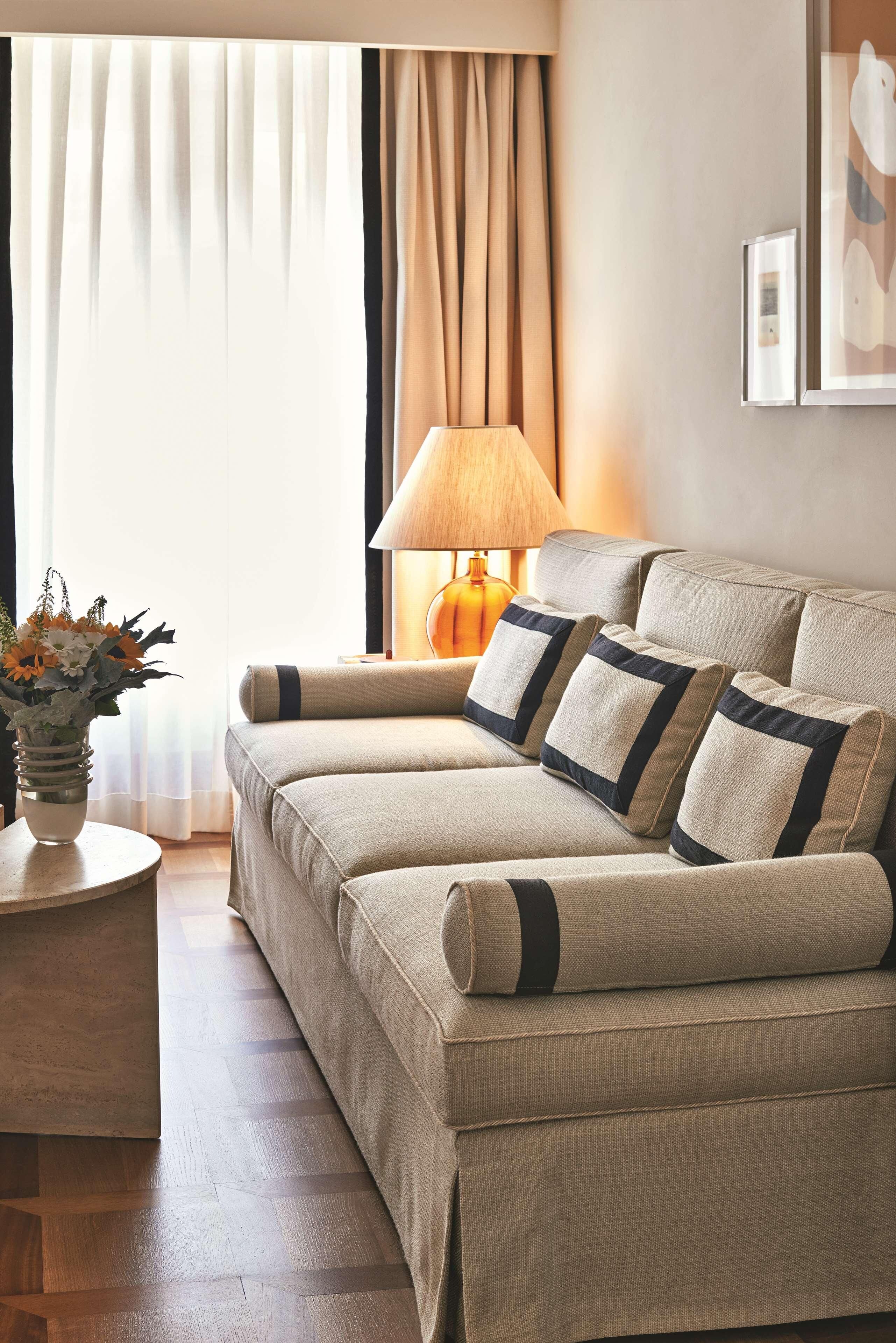 A living room with a beige sofa set, a round side table with a vase of flowers, and a lamp.