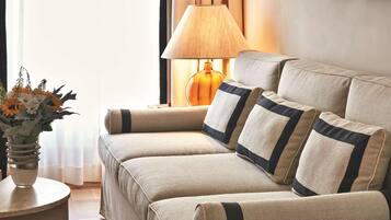 A living room with a beige sofa set, a round side table with a vase of flowers, and a lamp.