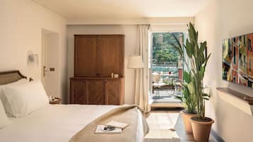 A hotel room with a bed, wooden wardrobe, potted plants, and a view of the outside balcony.