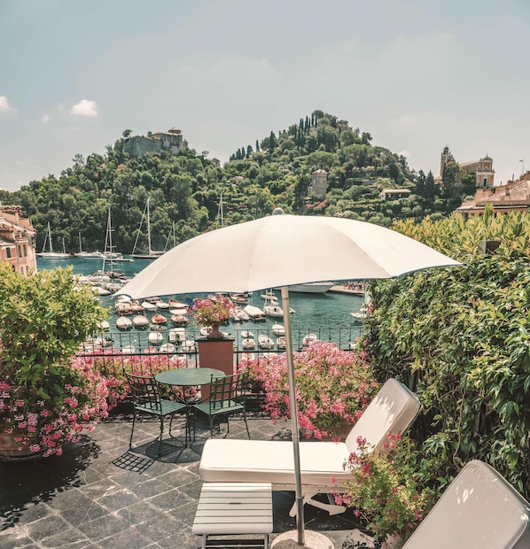 A terrace with a table and chairs, a lounge chair, and a large umbrella. - Splendido Mare, A Belmond Hotel, Portofino (Santa Margherita Ligure)