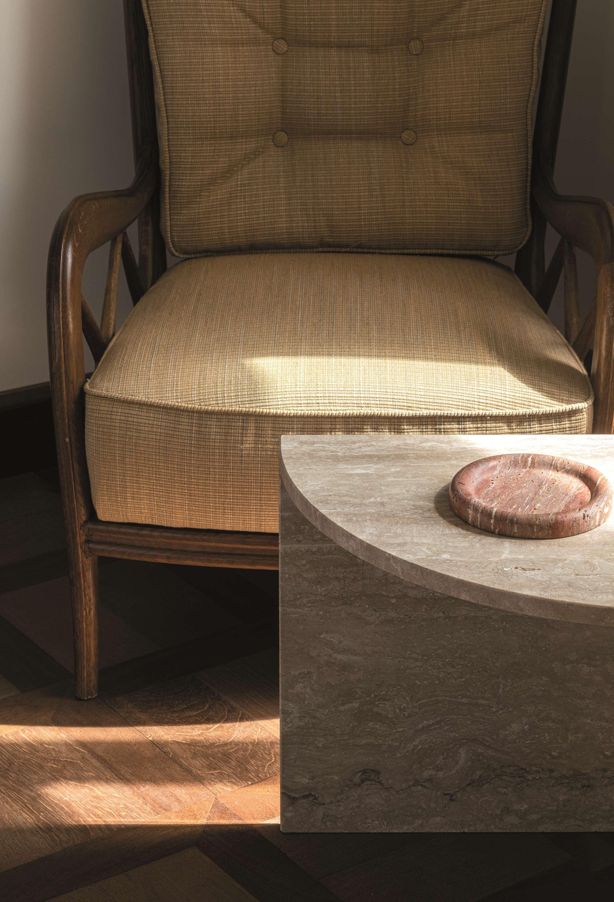 Una silla de madera con asiento y respaldo tejido, ubicada junto a una mesa redonda de piedra con un objeto circular encima.
