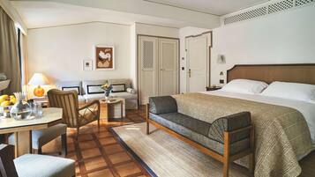 A hotel room with a bed, a sofa, a dining table with chairs, a lamp, and a decorative wall piece.