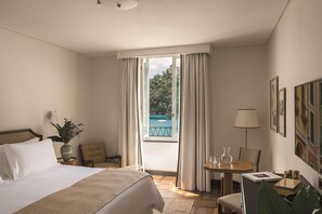 A hotel room with a bed, a small table with a lamp, a chair, a window with curtains, and a view of a pool. - Splendido Mare, A Belmond Hotel, Portofino (Santa Margherita Ligure)