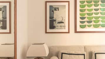 Una sala de estar con un sofá color beige, una pequeña mesa de madera con una lámpara y cuadros en la pared.