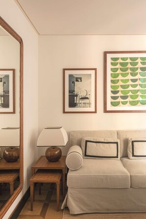 A living room with a beige sofa, a small wooden table with a lamp, and framed pictures on the wall. - Splendido Mare, A Belmond Hotel, Portofino (Santa Margherita Ligure)