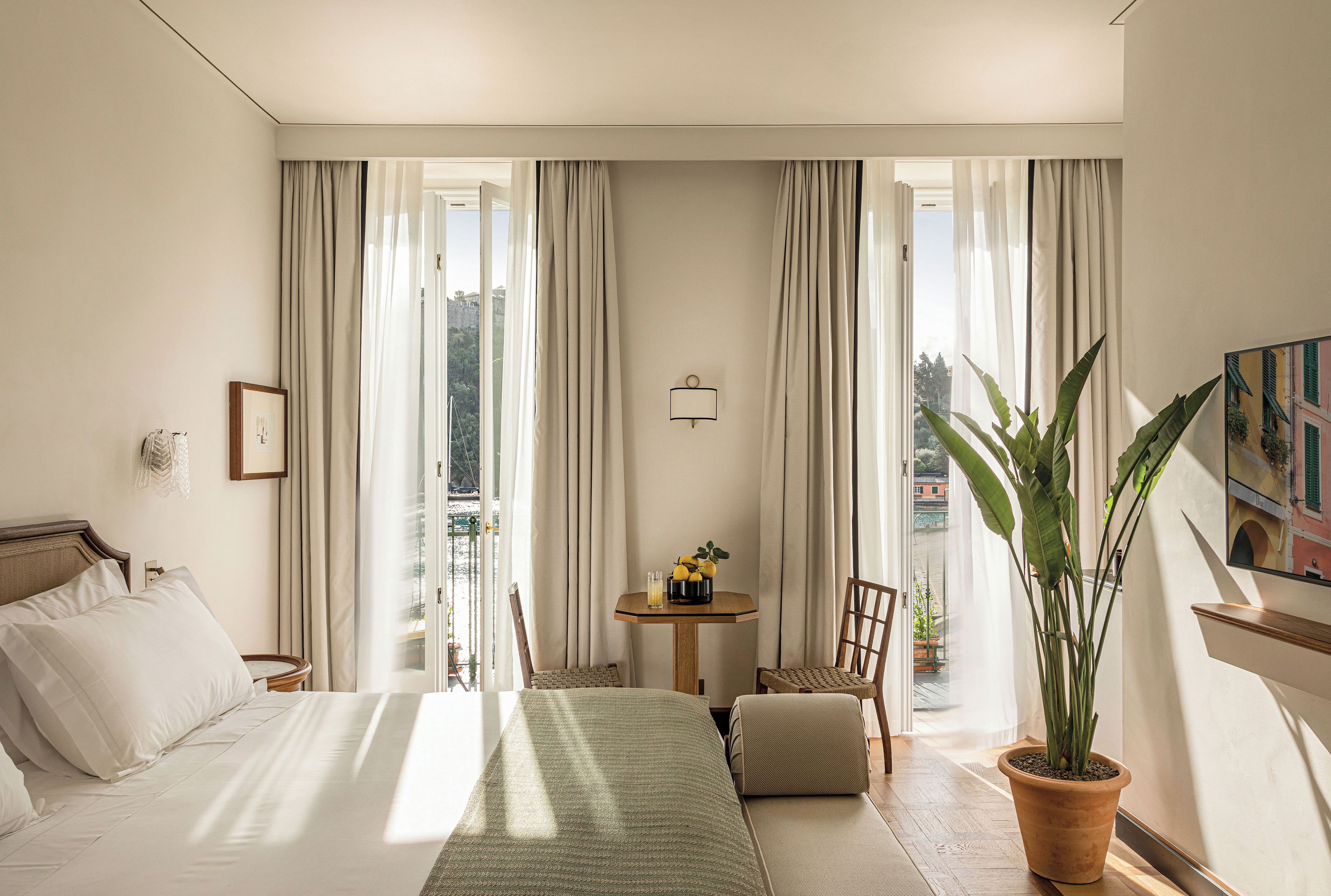 Ein Hotelzimmer mit Bett, einem kleinen Tisch mit Pflanze, einem Sessel und Blick ins Freie.