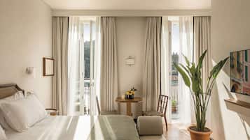 Ein Hotelzimmer mit Bett, einem kleinen Tisch mit Pflanze, einem Sessel und Blick ins Freie.