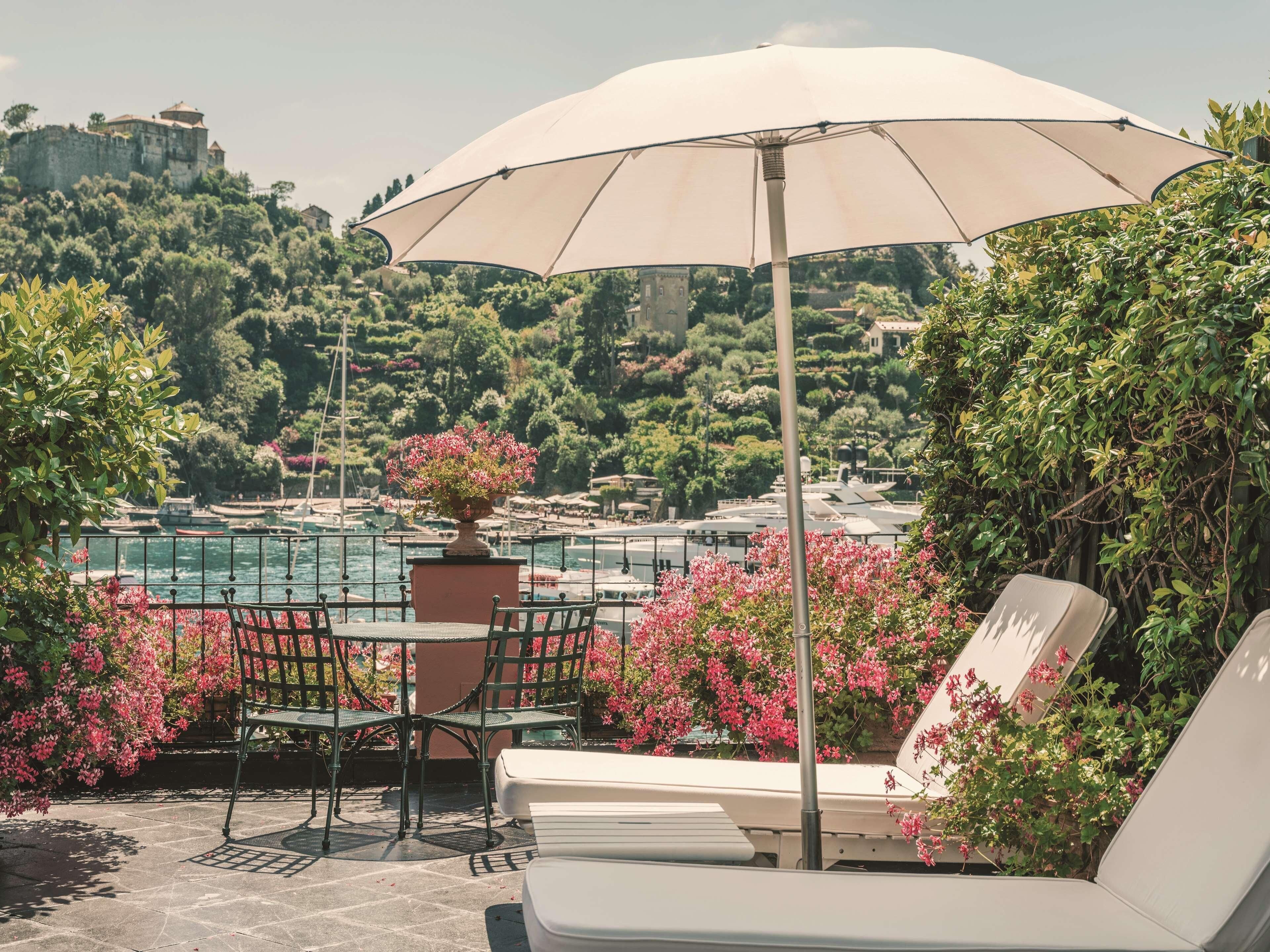 En terrasse med et bord og stole, en stor parasol og udsigt over vand og grøn bevoksning.