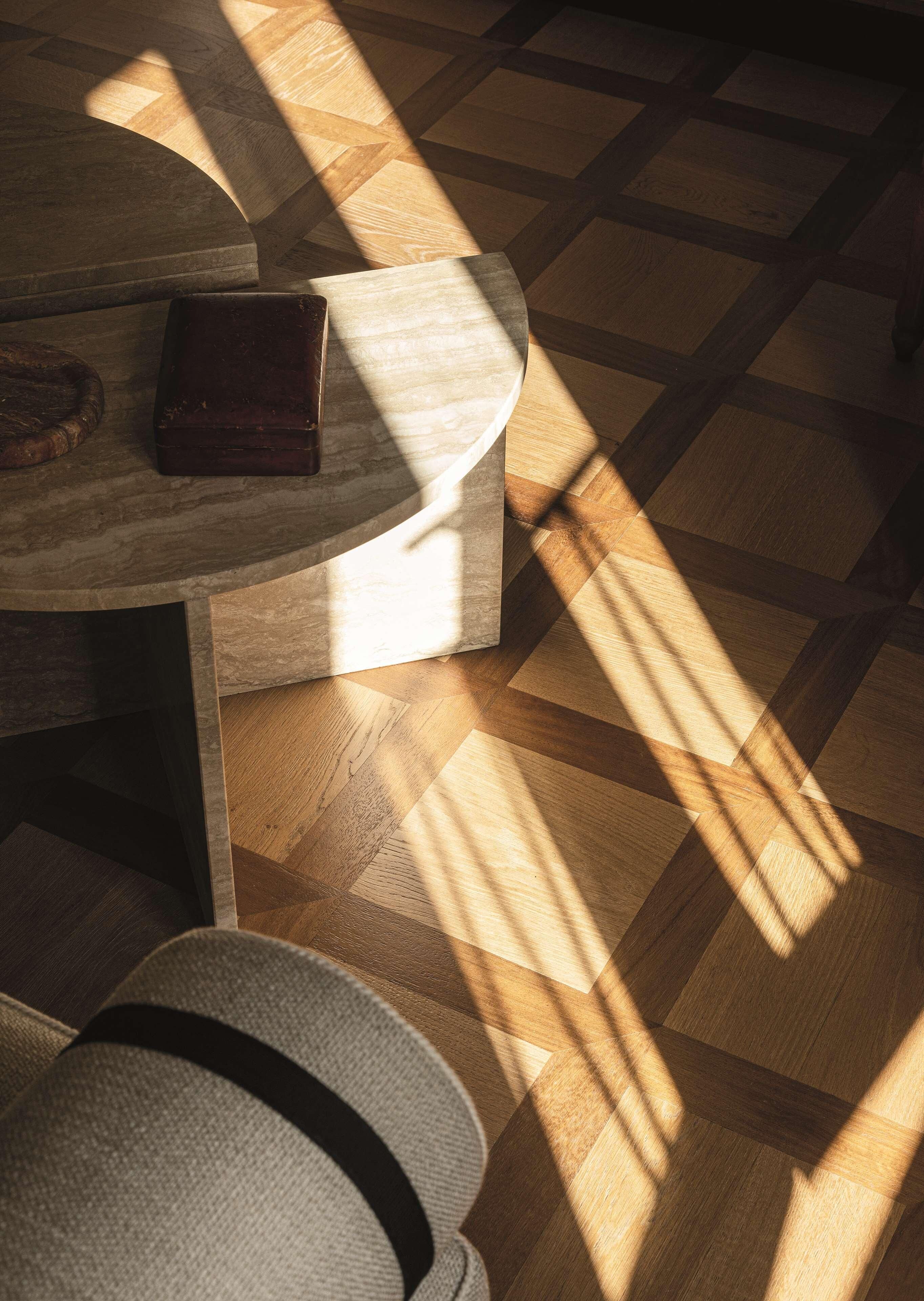 A wooden floor with a geometric pattern, a round table with a dark surface, and a hat on the floor.