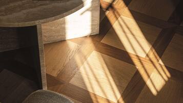 A wooden floor with a geometric pattern, a round table with a dark surface, and a hat on the floor.
