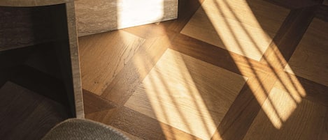 A wooden floor with a geometric pattern, a round table with a dark surface, and a hat on the floor.
