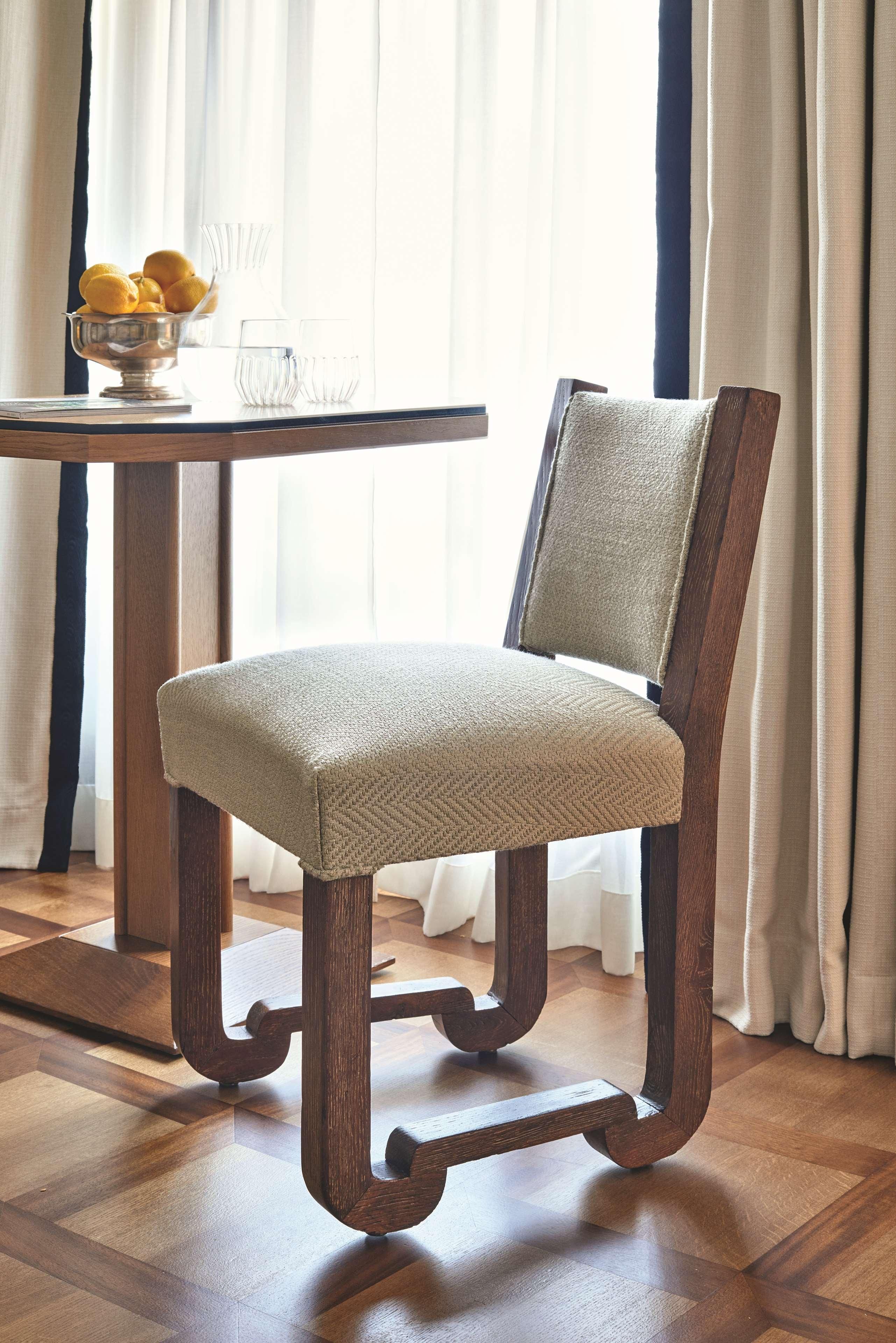 A wooden chair with a woven seat and backrest, positioned next to a table with a bowl of lemons and glasses.