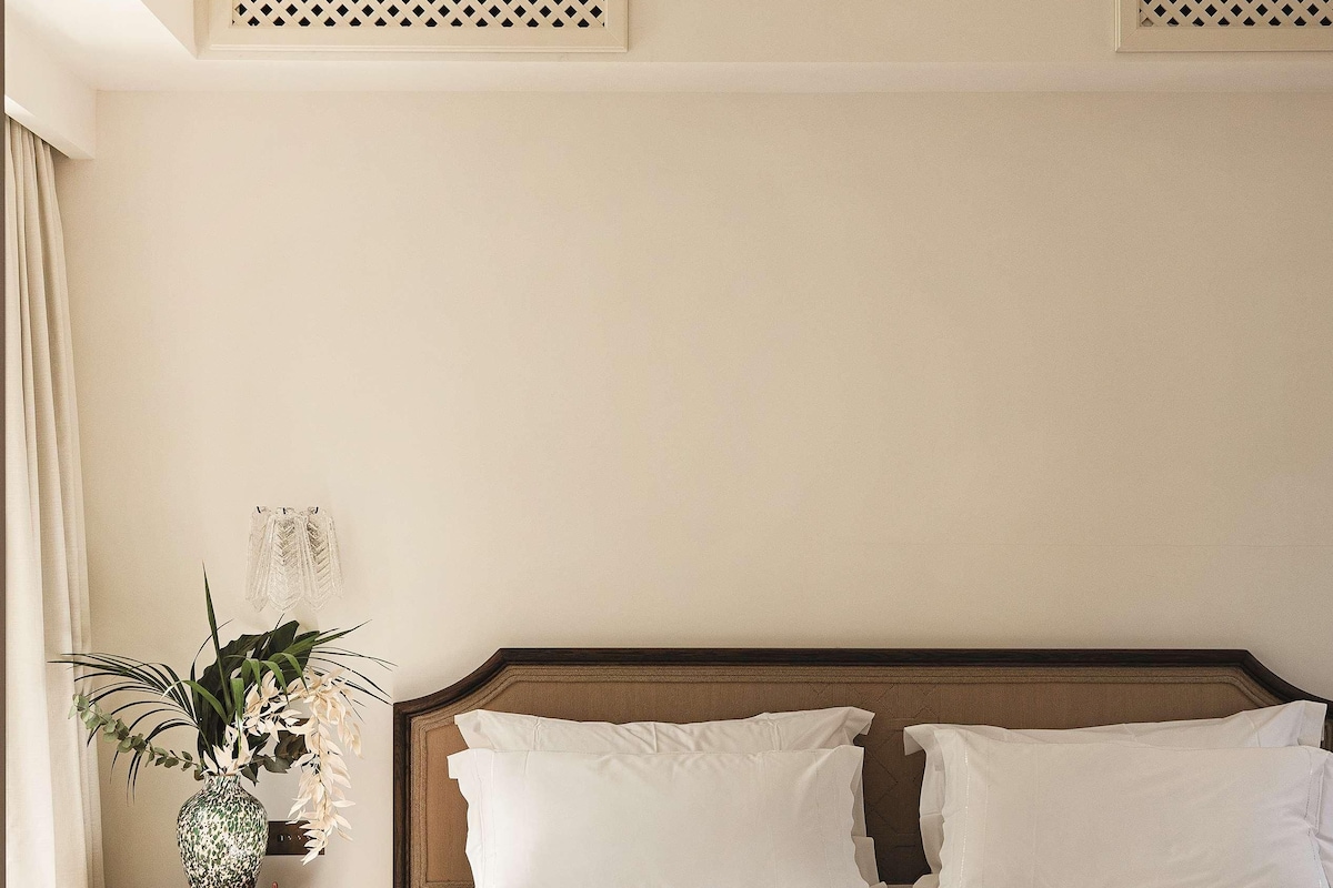 A neatly arranged bedroom with a wooden bed, a bedside table with a plant, and a bench at the foot of the bed.