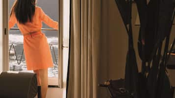 A woman in an orange dress standing by a window overlooking the sea.