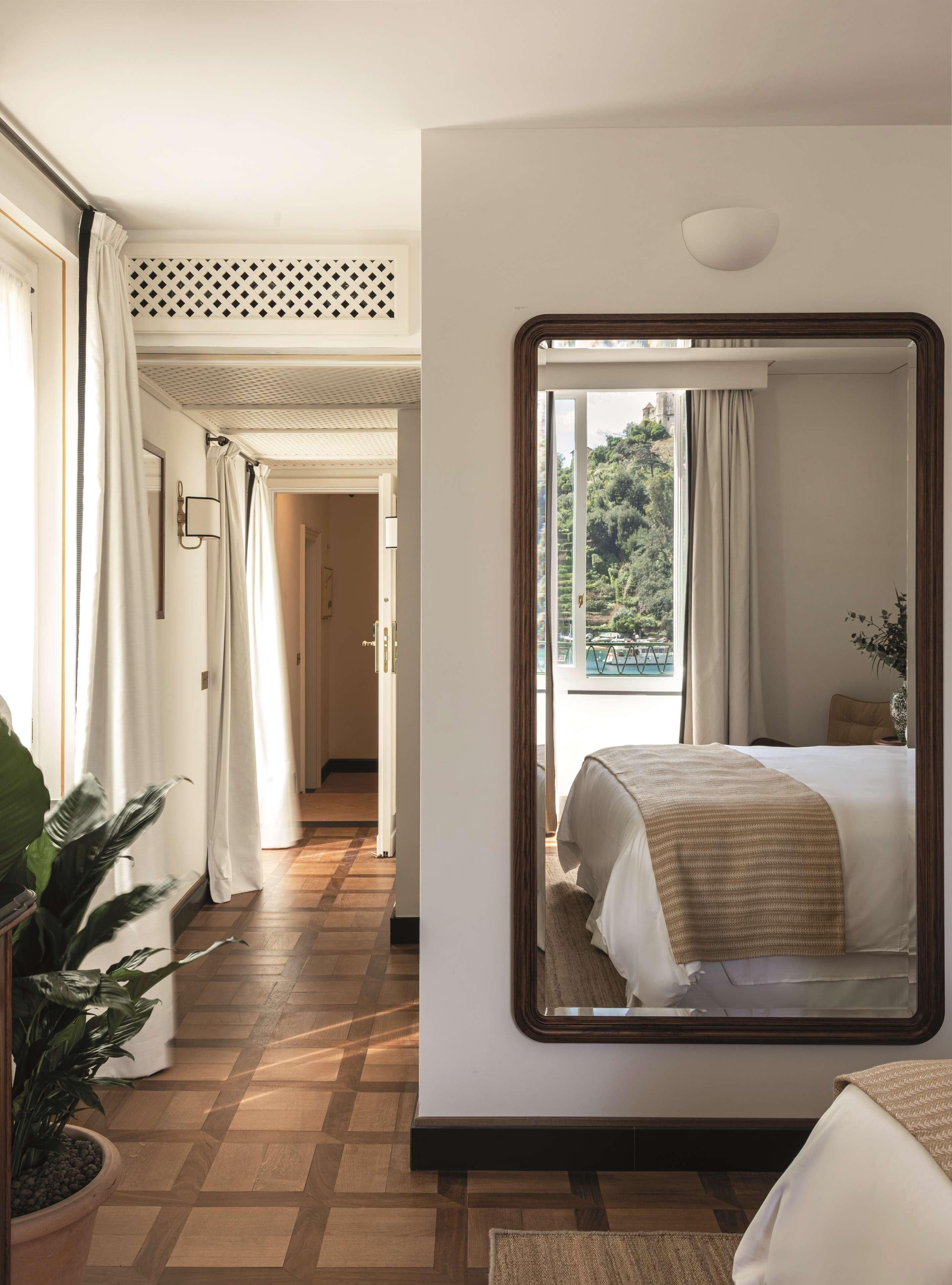 A hotel room with a large mirror reflecting the bed and a view of greenery outside.