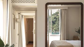 A hotel room with a large mirror reflecting the bed and a view of greenery outside.