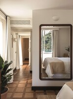 Una camera d'albergo con un grande specchio che riflette il letto e vista su del verde all'esterno.
