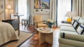 Habitación de hotel con cama, dos sillones, un sofá, una mesita con un jarrón de flores, una lámpara y un cuadro en la pared.
