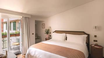 Habitación de hotel con cama, mesita de noche, sillón y vistas al balcón exterior.