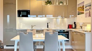 Eine moderne Küche mit Essbereich, ausgestattet mit einem weißen Tisch und Stühlen, Edelstahlgeräten und einem minimalistischen Design.