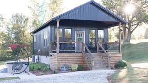 A wooden cabin with a porch, a small staircase, and a garden area with plants and a hammock.