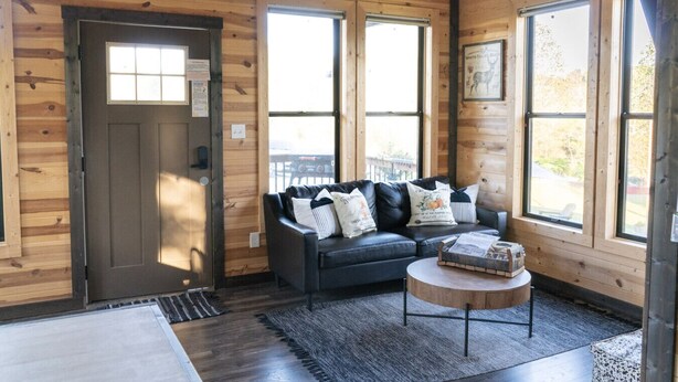 A cozy cabin interior with a dark leather sofa, a small wooden coffee table, and a door with a window.