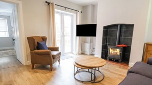 Una sala de estar con sofá, sillón, mesa de centro de madera, chimenea y televisor montado en la pared.