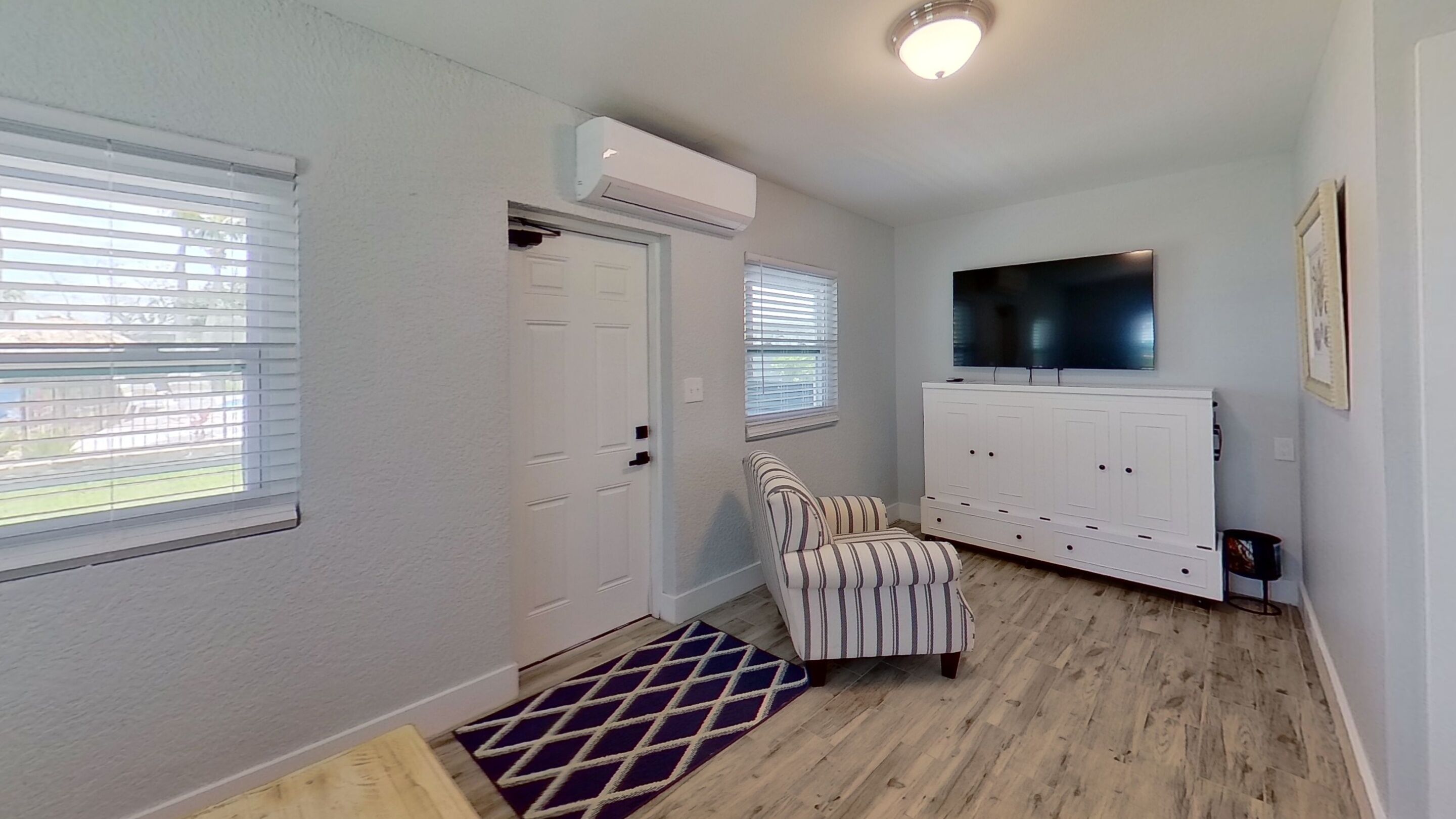 A room with a door, a striped chair, a TV on a cabinet, and a patterned rug.