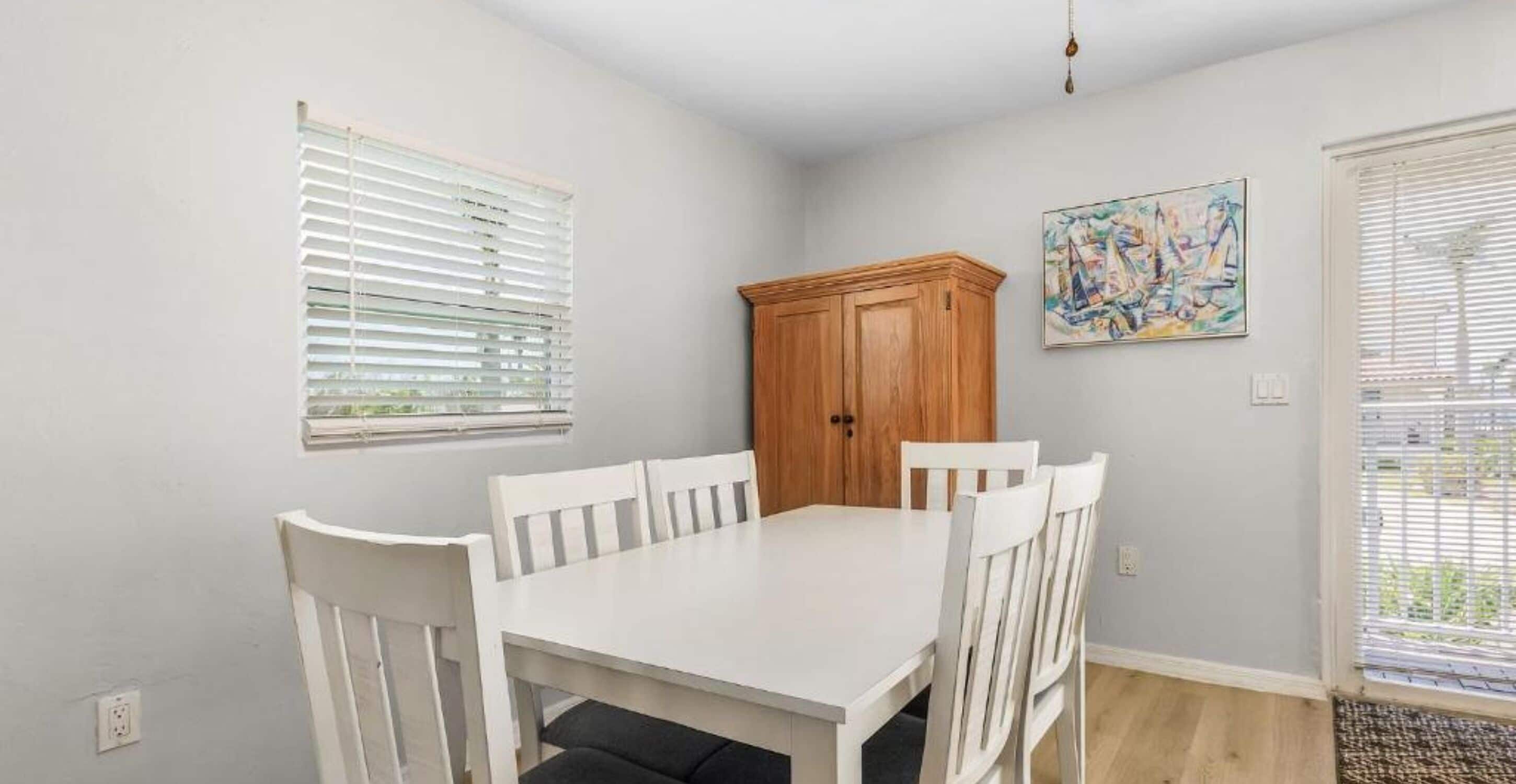 A dining area with a white table and chairs, a wooden cabinet, and a painting on the wall.