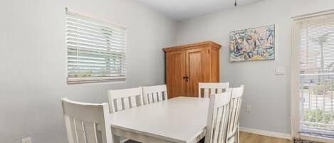 A dining area with a white table and chairs, a wooden cabinet, and a painting on the wall.