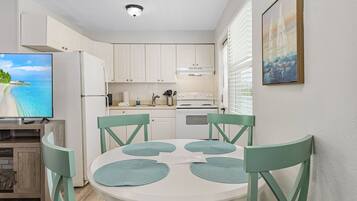 A compact kitchen with white cabinets, a built-in oven, and a dining area with a round table and green chairs.