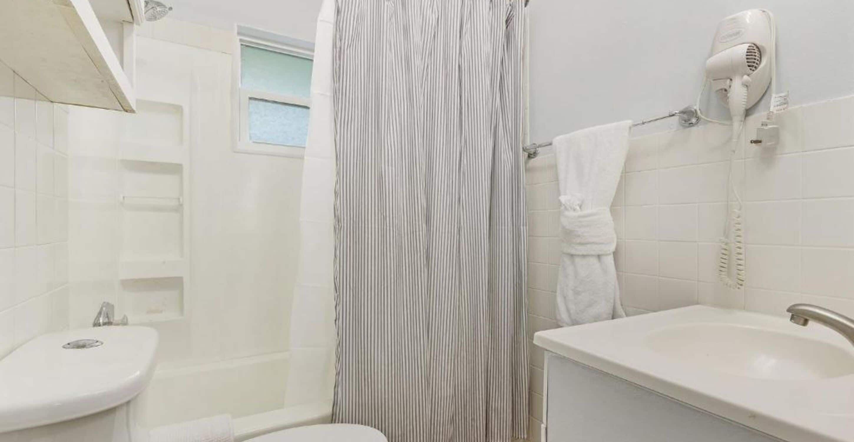 A bathroom with a white sink, a shower curtain, and a hairdryer mounted on the wall.