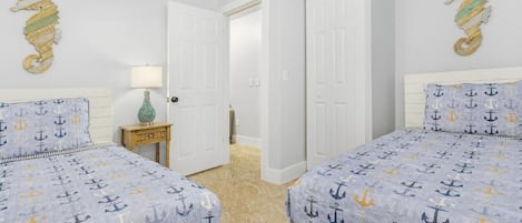 Un dormitorio con dos camas, cada una con una colcha azul con motivos de anclas, paredes blancas y decoración de caballitos de mar en la pared.