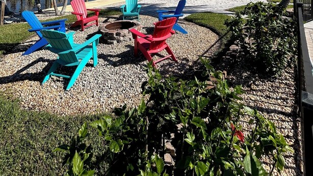 A beachside area with colorful Adirondack chairs, a fire pit, and a view of the water. - Matlacha on Shoreview (Cape Coral)
