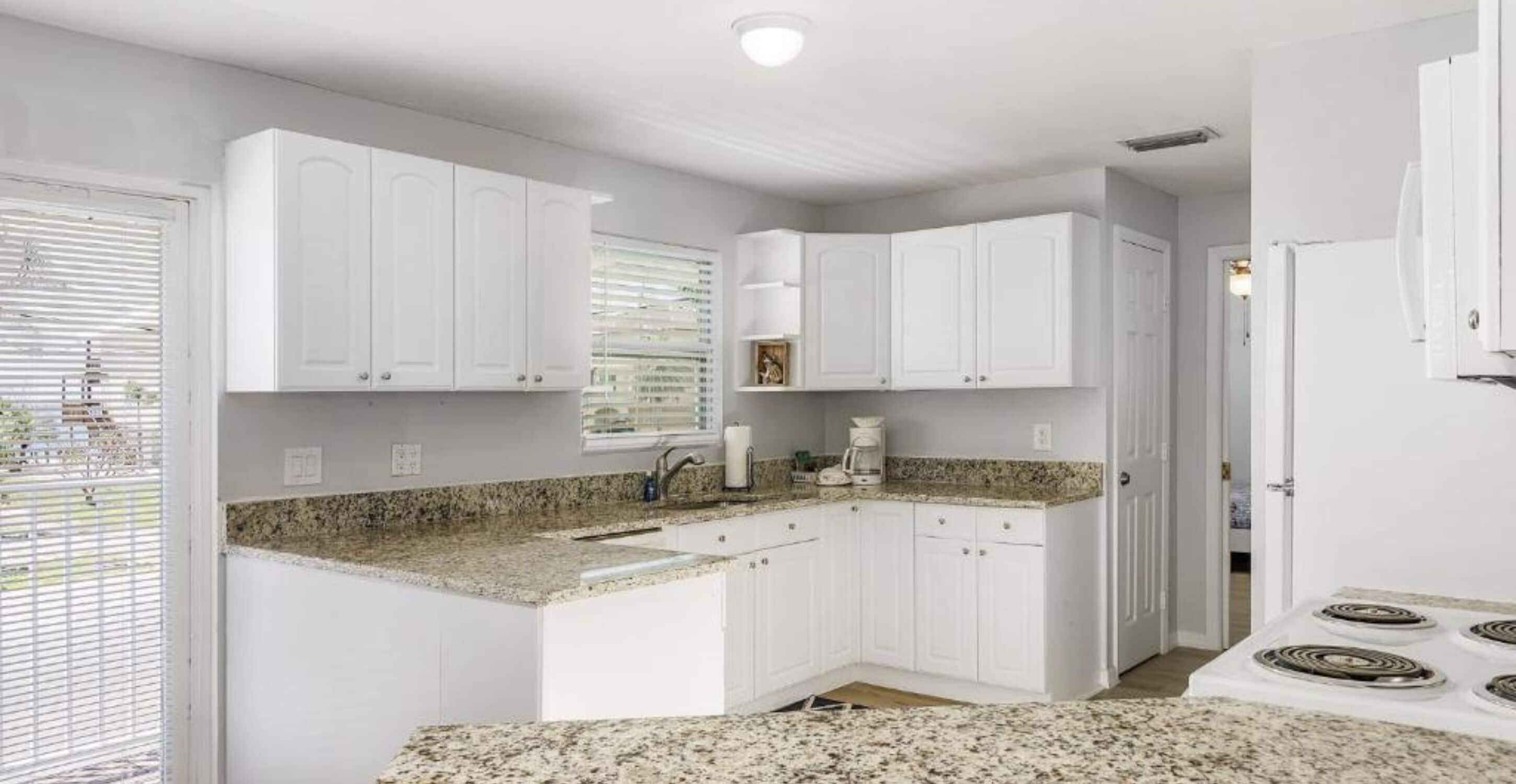 A modern kitchen with white cabinets, granite countertops, and a built-in stove.