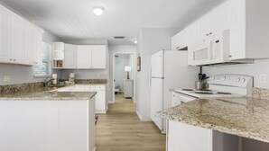A modern kitchen with white cabinets, granite countertops, a built-in oven, and a microwave. - Matlacha on Shoreview (Cape Coral)