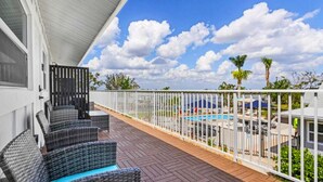 A balcony with wicker furniture, a pool, and a white fence. - Matlacha on Shoreview (Cape Coral)
