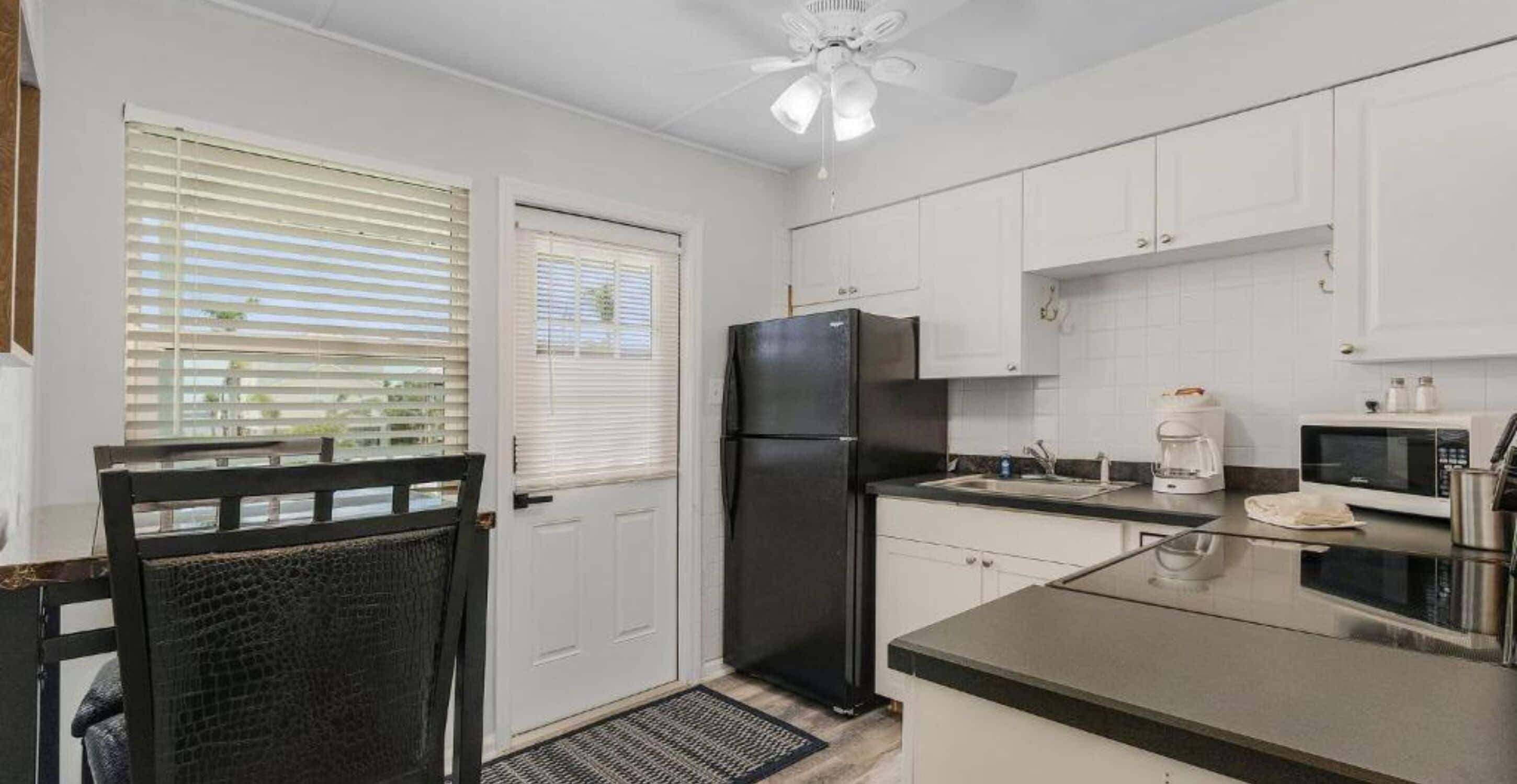 A compact kitchen with white cabinets, a black refrigerator, a microwave, and a coffee maker.