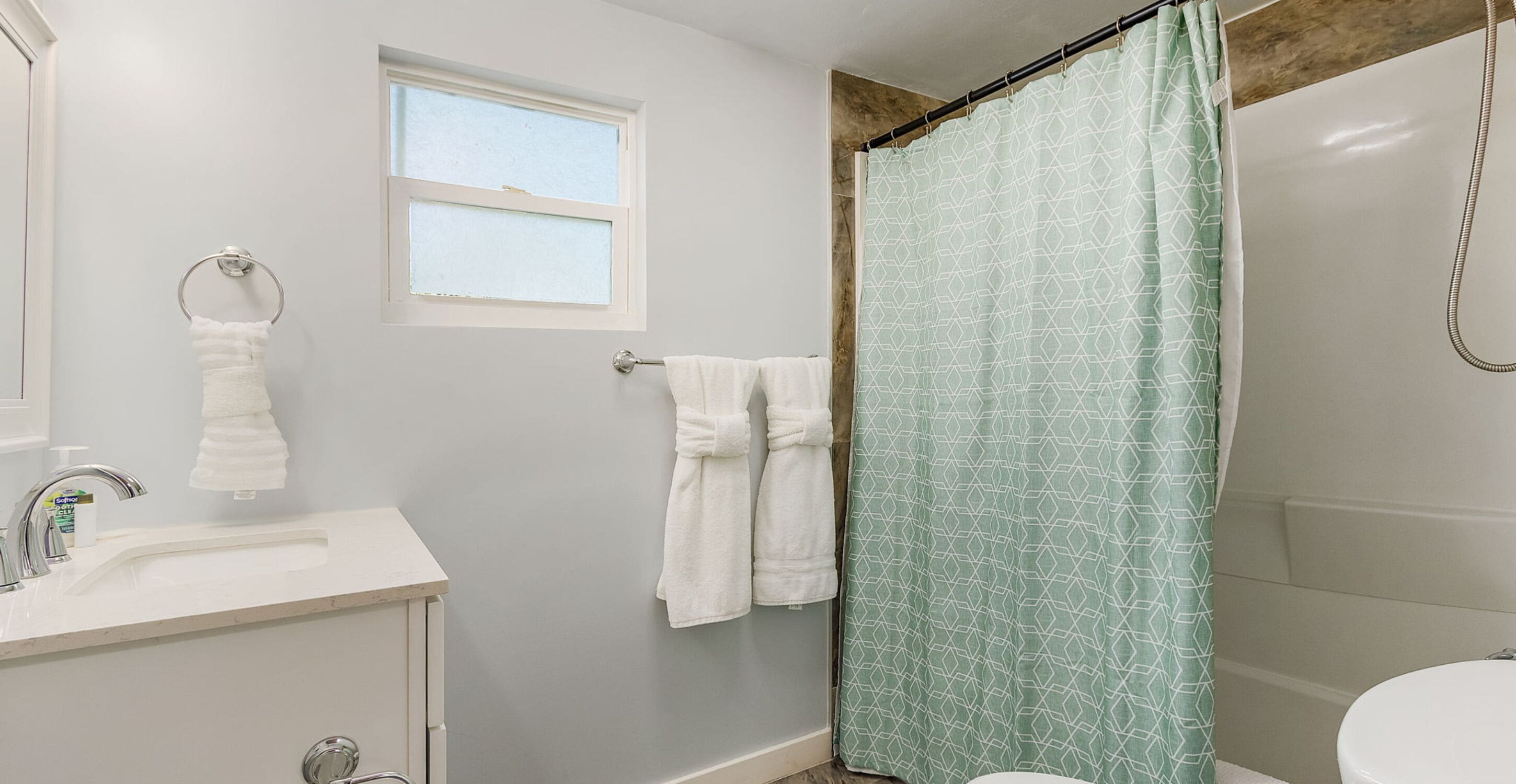 Une salle de bain avec un lavabo, un miroir, une fenêtre et un rideau de douche.