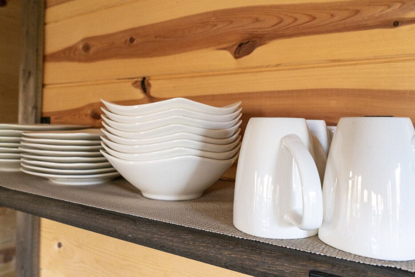 Una estantería de madera con platos y tazas de cerámica blanca.
