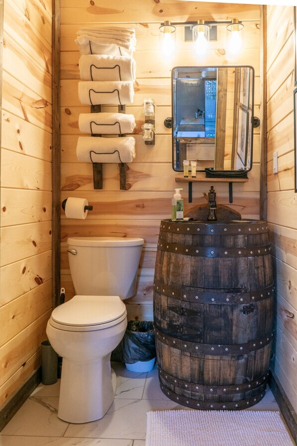 A wooden bathroom with a toilet, a large barrel sink, and a mirror.
