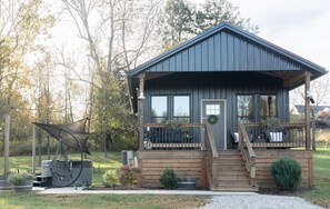 A rustic cabin with a wooden deck, a covered porch, and a small staircase leading to the entrance.