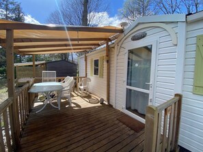 A covered deck with a table and chairs, a sliding door, and a small window. - Mobile Homes at Camping Parc des Roches (Saint-Chéron)