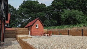 Ein rustikales, rotes Backsteinhaus mit geneigtem Dach, einer Holzterrasse und einer Außenbereich-Sitzgelegenheit mit Stühlen.