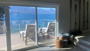 Una stanza con una porta a vetri scorrevoli che dà su un balcone con vista sul mare e sulle montagne. Sul balcone si trovano due poltrone in vimini e un tavolino.