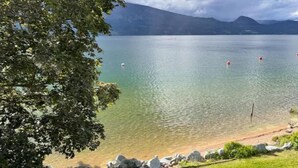 Una vista limpida su un lago, con un muro di pietra e un'area erbosa in primo piano, e montagne sullo sfondo.