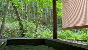 A hot tub in a forested area with a view of dense greenery. - Takara Onsen Pension Satchimo (Kitashiobara)