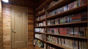 A wooden-paneled room with a bookshelf filled with books. - Takara Onsen Pension Satchimo (Kitashiobara)